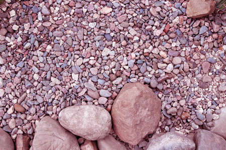 Big round stones and small pebbles of different shape and in different shades of pink color as a...