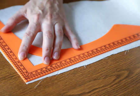 Working process of a dressmaker. Closeup photo of person's hand, marking line on fabric and triangle...