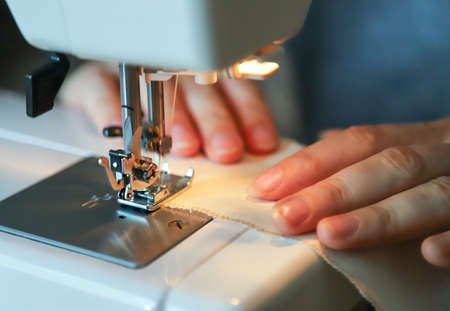 Working process of a tailor. Craftsperson sews with a sewing machine. Closeup photo.