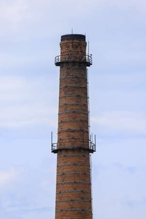 An old brick industrial plant chimney against a cloudy sky