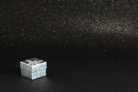 Silver gift box with white ribbon on black sparkling glittery background. Photo in perspective with...