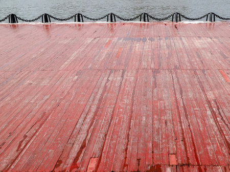An old wet wooden embankment painted in red on a rainy spring day. Photo in perspective with selective focusの写真素材