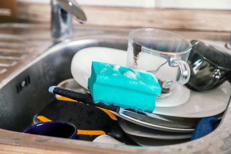 Washing dishes by hand. Closeup of the pile of dirty dishes and the soapy sponge in stainless steel kitchen sinkの写真素材
