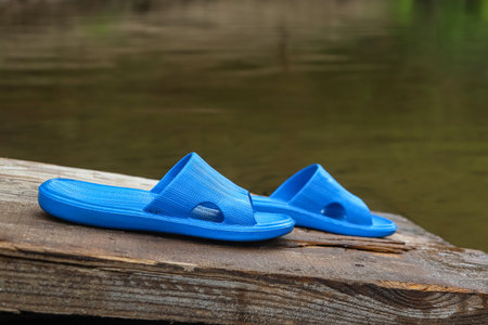 Closeup of a pair of blue rubber slippers standing near water on wooden gangway plank. Summer beach...