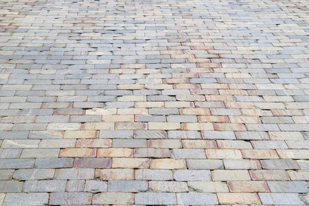 Old damaged sidewalk paved with gray and orange rectangular stone tiles with brown stains in perspective. Photo with selective focusの写真素材