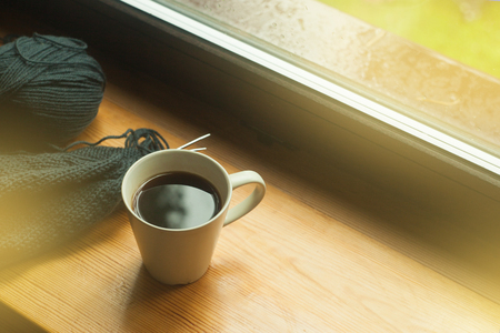 Cup of coffee and knitting on windowsill, cozy morning, toned photoの写真素材
