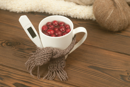 Cup of tea with cranberries, scarf, thermometer - the concept of seasonal respiratory diseases,...