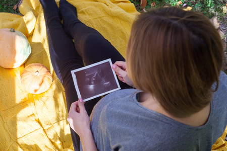 young pregnant woman looking at ultrasound image in autumn sunny day outdoorの写真素材