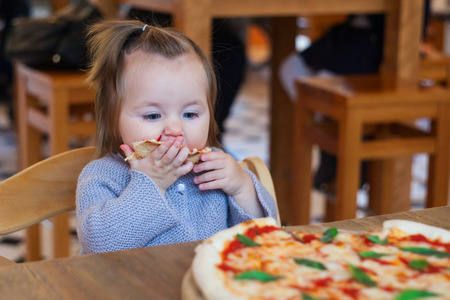 Cute funny little girl eating spaghetti in cafe
