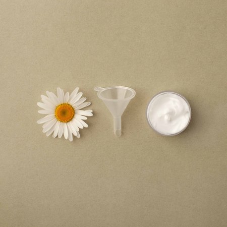 Herbal spa cosmetic cream with camomile flowers hygienic skincare lotion product wellness and relaxation makeup mask in glass jar on green pastel backgroundの写真素材