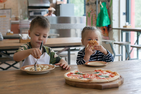 kids eat pizza and meat dumplings at cafe. children eating unhealthy food indoors. Siblings in the cafe, family holiday concept.の写真素材