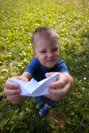 Happy laughing child hold paper ship indoors. Green field background. Happy childhood, summer, holiday, travel, vacation conceptの写真素材