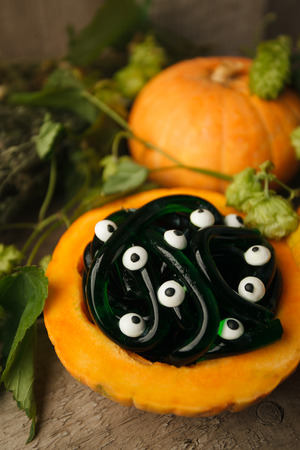 Spooky Halloween party food - gummy jelly worms in pumpkin with monsret eyes on wooden background, holiday party close upの写真素材
