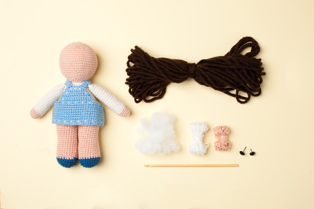 a toy crocheted, a doll in a blue dress, an unfinished work - the hair is not sewn and the decor is not executed, the tools and materials lie nearbyの写真素材