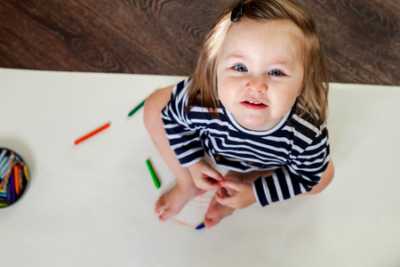 1 year old girl sitting on the floor with pencils and paper, looking at the cameraの写真素材