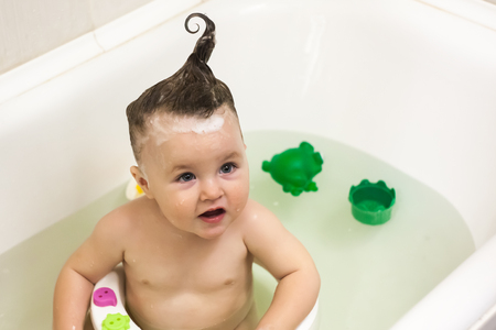 Blue eyes little girl in the bathing bucket looking and smiling. Happy baby having a bath and playing with rubber toys.の写真素材