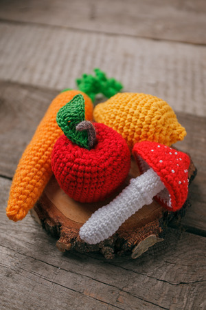 Set of knitted toys lemon, carrot, apple, amanita on wooden background. Earlier tactile development of children, craft toys, vegetarian menu concept, copy spaceの写真素材
