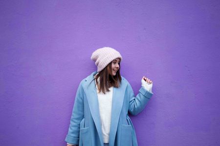 Horizontal portrait of pleasant Caucasian female with brown hair, wearing blue casual coat and warm woolen hat, looking happily in rightの写真素材