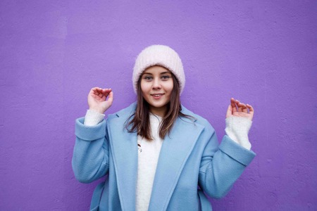 Horizontal portrait of pleasant cute Caucasian female with brown hair, wearing blue casual coat and warm woolen hat, looking happily in cameraの写真素材