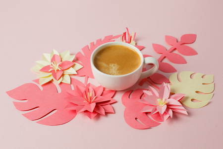 White cup of espresso on a pink pastel with modern origami paper craft decor flowersの写真素材