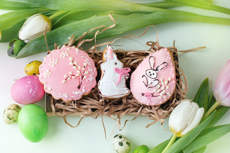 Colorful Easter cookies with frosting icing decor, painted colorful eggs and tulips on light table.