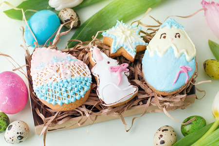 Colorful Easter cookies with frosting icing decor, painted colorful eggs and tulips on light table.の写真素材