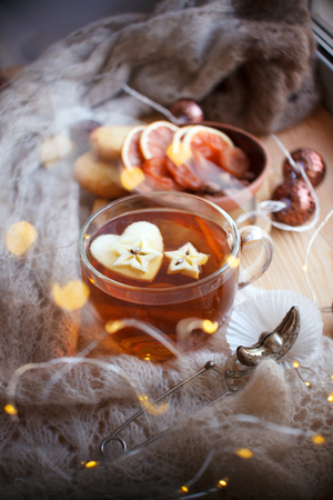 still life tea drinking in the living room. Cup of tea with apple and garland light wooden table, the concept of coziness, calmness, autumn winter weekend and holidayの写真素材
