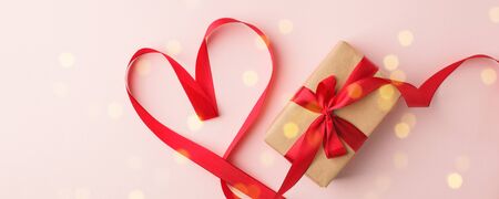 Present or gift box, satin red ribbon heart on pink background top view. Valentines day greeting card. Flat lay style. Concept of seasonal roance holiday, sale, coupon bannerの写真素材