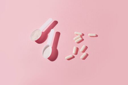 Protein powder, scoop, energetic muesli bars, vitamin pills, gainer on pinkの写真素材