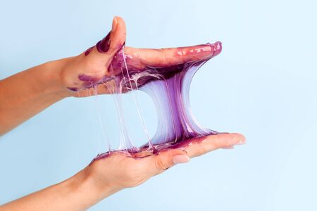 Young girl hands with sticky purple slime on blue background, liqiud wax for depilation, conceptual...