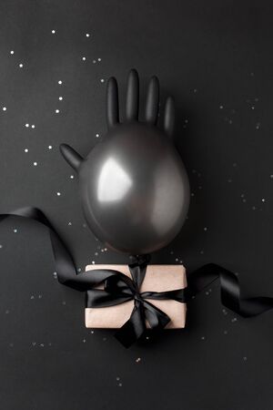 Craft gift box on dark background, decorated with balloon from medical glove and bow. For birthday, anniversary presents, gift post cards in period of coronavirus pandemic and self isolationの写真素材