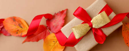Autumn creative holiday present. Handmade paper gift box with satin bow, foliage dried leaves on...