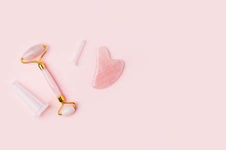 Pink Gua Sha Stone, roller facial massage tools. Rose Quartz jade roller and stone on pink background. Anti age, lifting and toning treatment at home. Copy spaceの写真素材