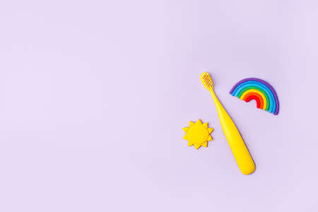Yellow Cute kids toothbrush, sun, rainbow on pastel purple background. Dental and healthcare concept, copy space, 90s, 80s style design, bright flyer for dental clinicの写真素材