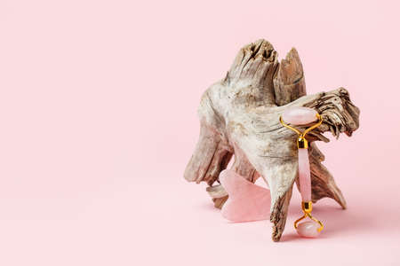 Gua Sha pink quartz massager and jade roller on pink pastel background. Jade stone for face and body care. Horizontal shoot, woody plant root, stylish trendy creative card with copy spaceの写真素材