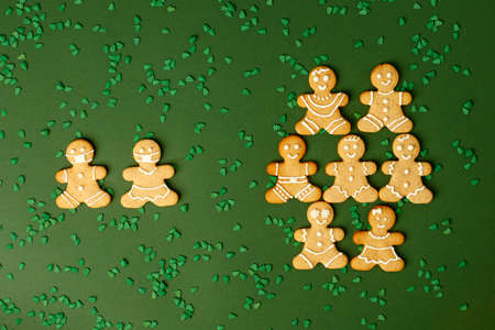 Happy New Year's set of cookies, gingerbread man in face mask against group of men from ginger biscuits glazed sugar decoration on green background, minimal seasonal pandemic winter holiday conceptの写真素材