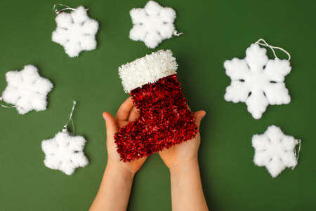 Kids hands holding decorative red Christmas sock on natural green background. Sale, Holiday, greering card Happy new year, Merry Christmas, banner for your site, invitation, flyer, holiday cardの写真素材