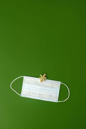 Trendy set for party in term of coronavirus pandemic - medical mask and seasonal decoration snowflake on natural shades of green background, New normal New year, Christmas holiday conceptの写真素材