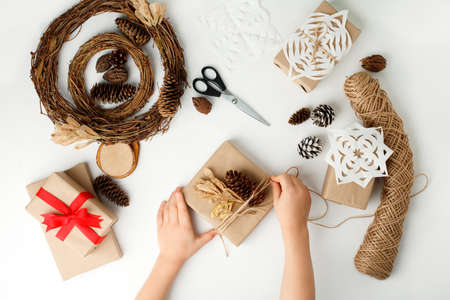 Child's hands making Christmas gift. Flat lay, top view, Kid hands wrapped gift box in craft paper,...