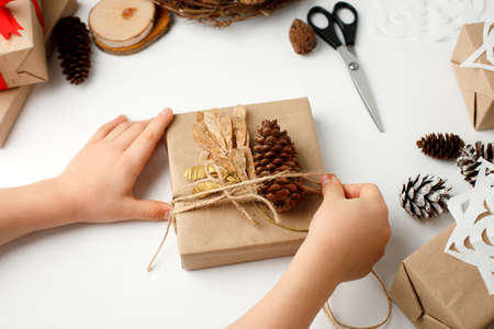 Kid hands wrapped gift box in craft paper, natural decoration details, zero waste packaging on white...
