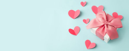 Stylish gift box with big pink bow and tender paper craft pink hearts on blue background, copy space, Greeting card, banner, flyer, postcard for Saint Valentine day, romance holiday, wedding, birthdayの写真素材
