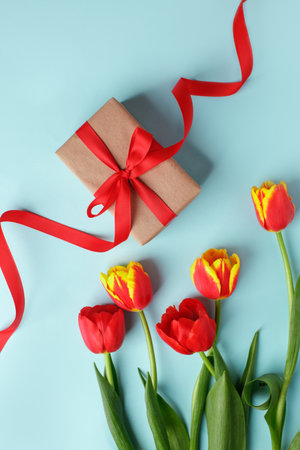 Yellow red tulip flowers bouquet and gift box on blue, copy space. Banner for seasonal holiday, springtime concept, International Woman da, 8 march, Happy Easter greeting flyer, invitationの写真素材