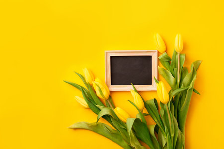 Beautiful spring Esater or holiday greeting card. Bouquet of yellow tulips and frame for your text on bright yellow table top view. Flat lay, banner for site, seasonal flyer, invitationの写真素材