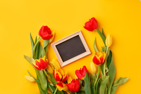 Beautiful spring Esater or holiday greeting card. Bouquet of red yellow tulips and frame for your text on bright yellow table top view. Flat lay, banner for site, seasonal flyer, invitationの写真素材