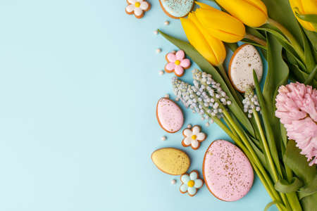 Happy Easter. Multi-colored pastel easter cookies gingerbread, seasonal flowers tulips on blue background. Easter concept, copy space, flyer, banner, coupon, greeting card, invitationの写真素材