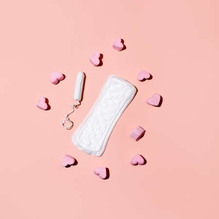 Tampons, feminine sanitary pads and cute heart candy on a pink background. Hygiene care during critical days. Menstrual cycle. Caring for women's health. Monthly protection, copy spaceの写真素材