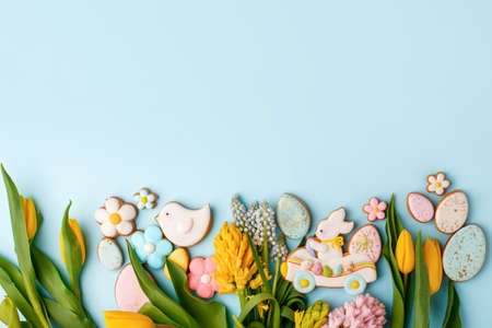 Happy Easter. Multi-colored pastel easter cookies gingerbread, seasonal flowers tulips on pastel blue background. Easter concept, copy space, flyer, banner, coupon, greeting card, invitationの写真素材