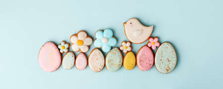 Sweets, pastry, gingerbread cookies for Easter table. Easter eggs, bird and tender simple flowers on blue background top view copy space, spring seasonal holiday banner for your sute, flyer, couponの写真素材