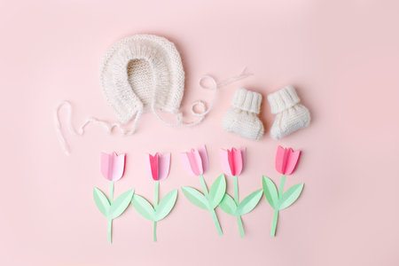 Bonnet and booties on a pink background. Handmade clothes for a newborn, decorative paper flowers. Newborn baby gift concept, mom's day, first birthday, first wardrobe, outfitの写真素材