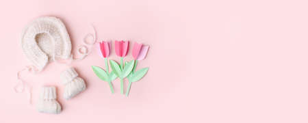 Bonnet and booties on a pink background. Handmade clothes for a newborn, decorative paper flowers. Newborn baby gift concept, mom's day, first birthday, first wardrobe, outfitの写真素材